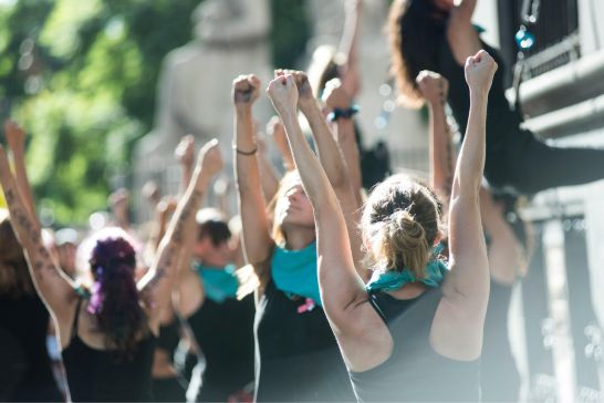 viele Frauen die beide arme zur Faust geballt nach oben strecken.